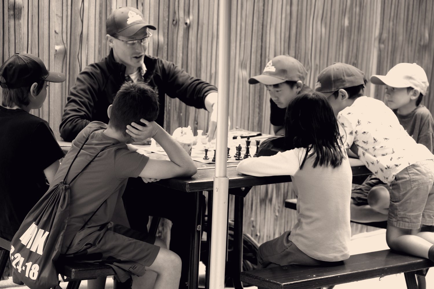 Children playing chess at an outdoor table during a Vellotti summer camp.