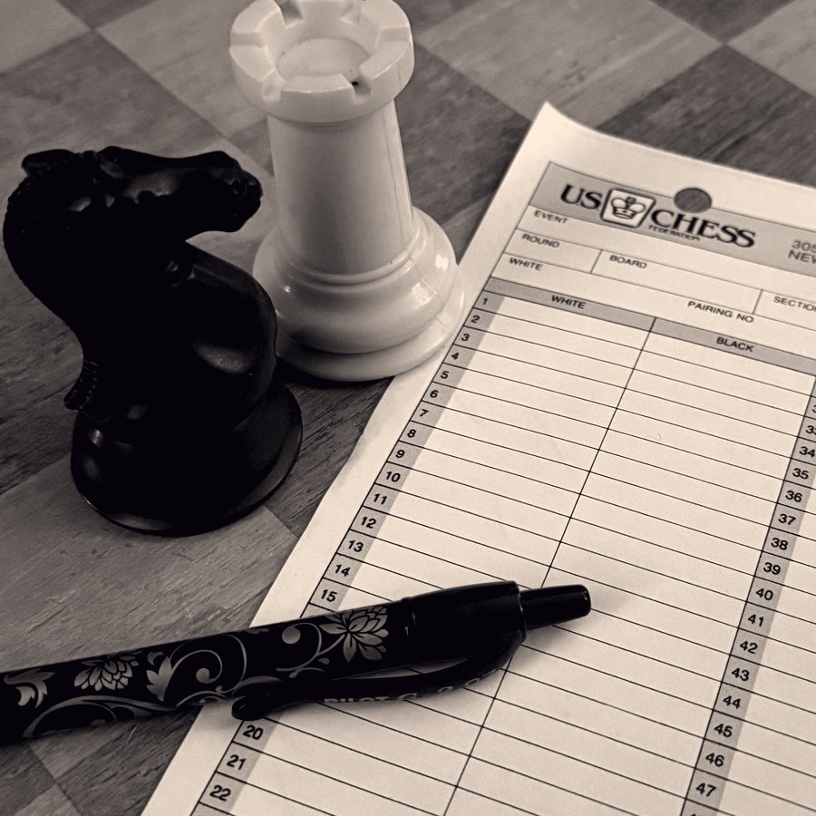 A US Chess Federation notation sheet beside a knight and a rook, with a pen resting on it.