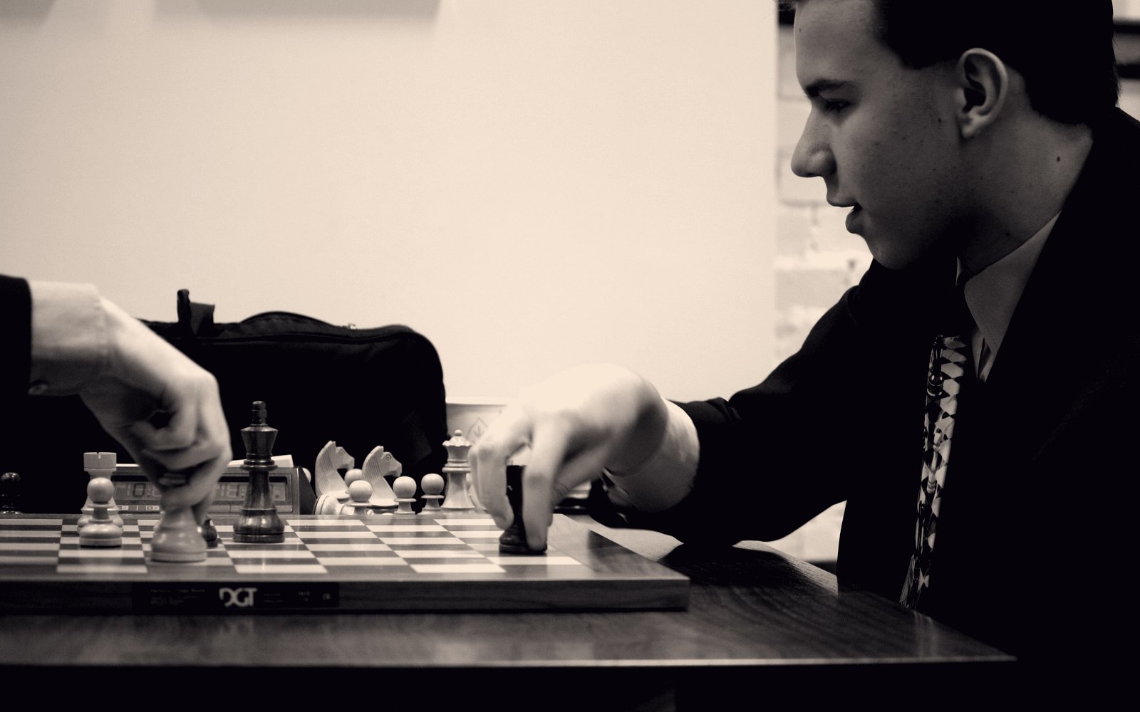 Luke Vellotti in a suit, reaching to move a piece during a tournament game.