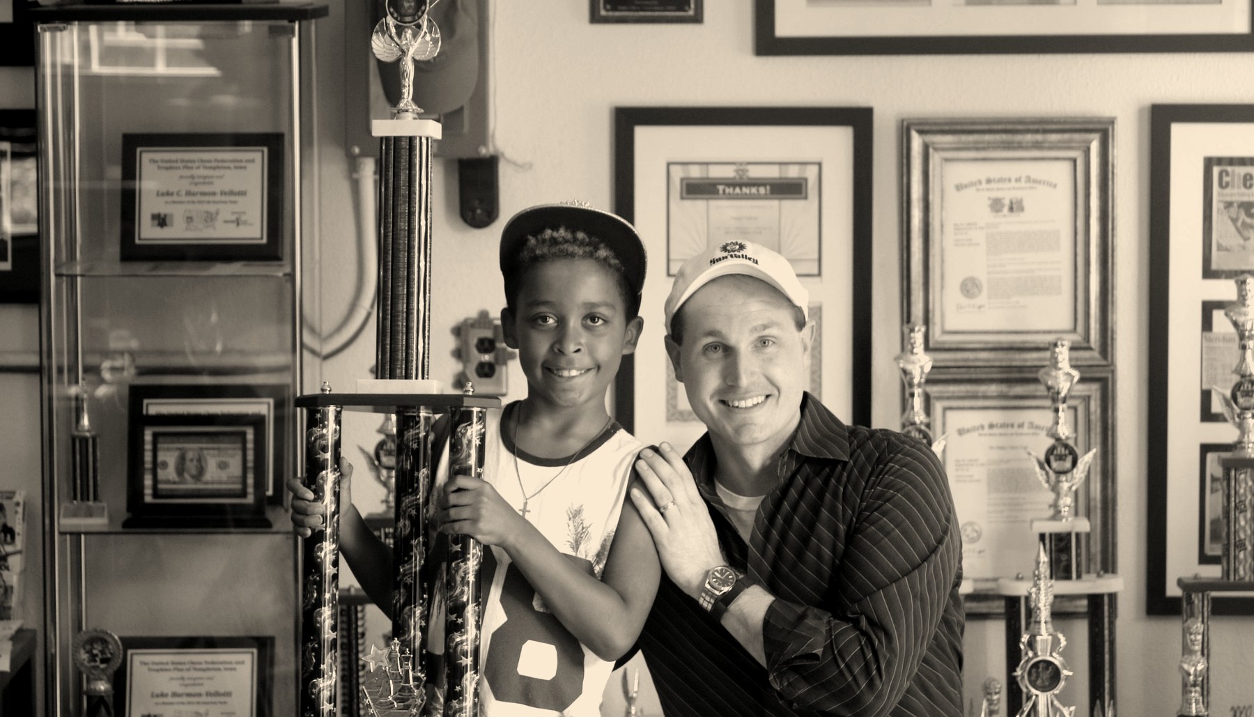 Daniel Vellotti with a young student holding a large trophy, in a room lined with trophies and framed certificates.